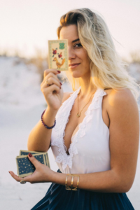 Blonde woman showcasing tarot card, standing outdoors, creating a mystical vibe.